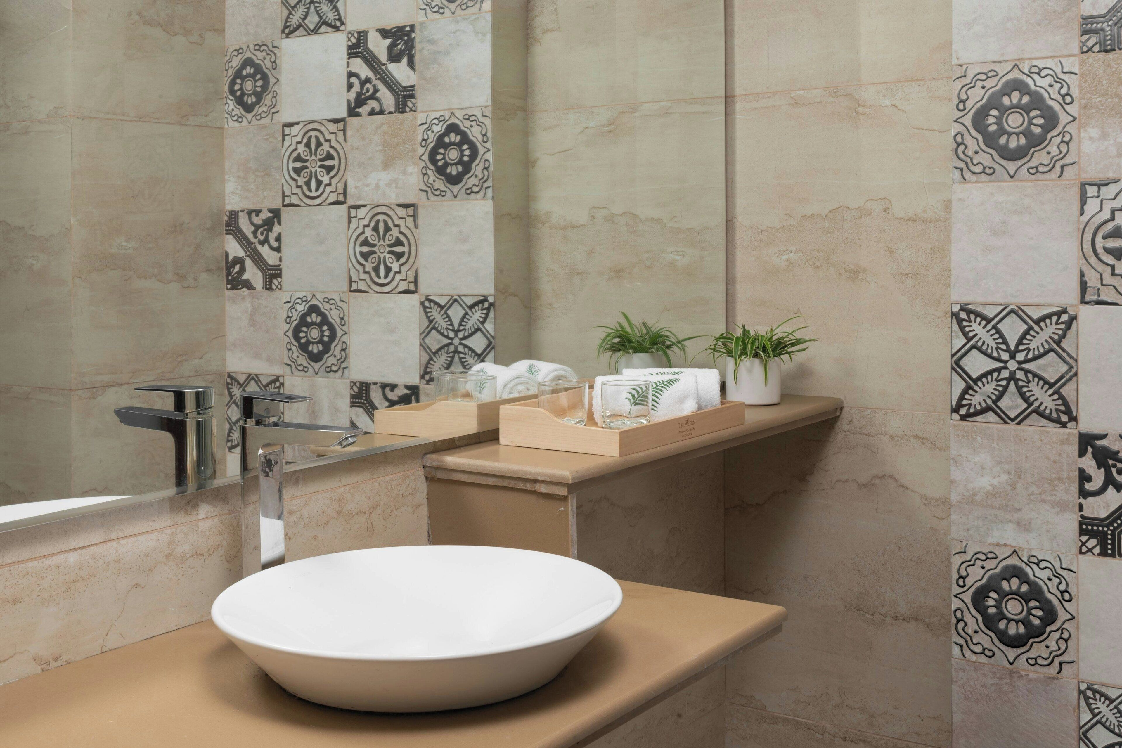 A bathroom with a large white basin, a mirror, a towel rack, and a shelf with toiletries.