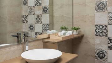 A bathroom with a large white basin, a mirror, a towel rack, and a shelf with toiletries.