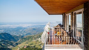 Un balcón con mobiliario de mimbre y techo de madera con vistas a un paisaje montañoso.