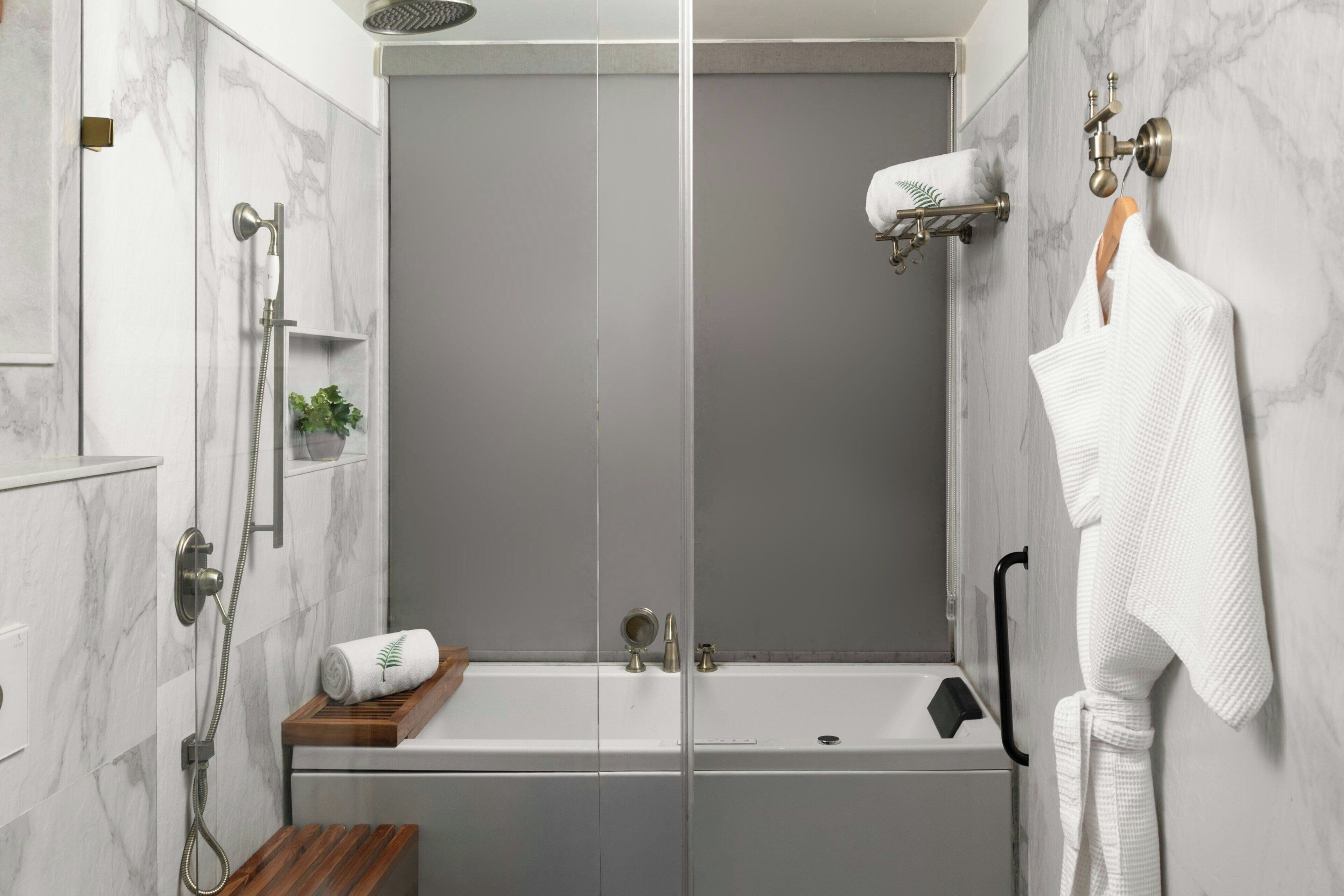 A modern bathroom with a glass-enclosed shower, a wooden bench, a towel rack, and a small shelf with a plant.