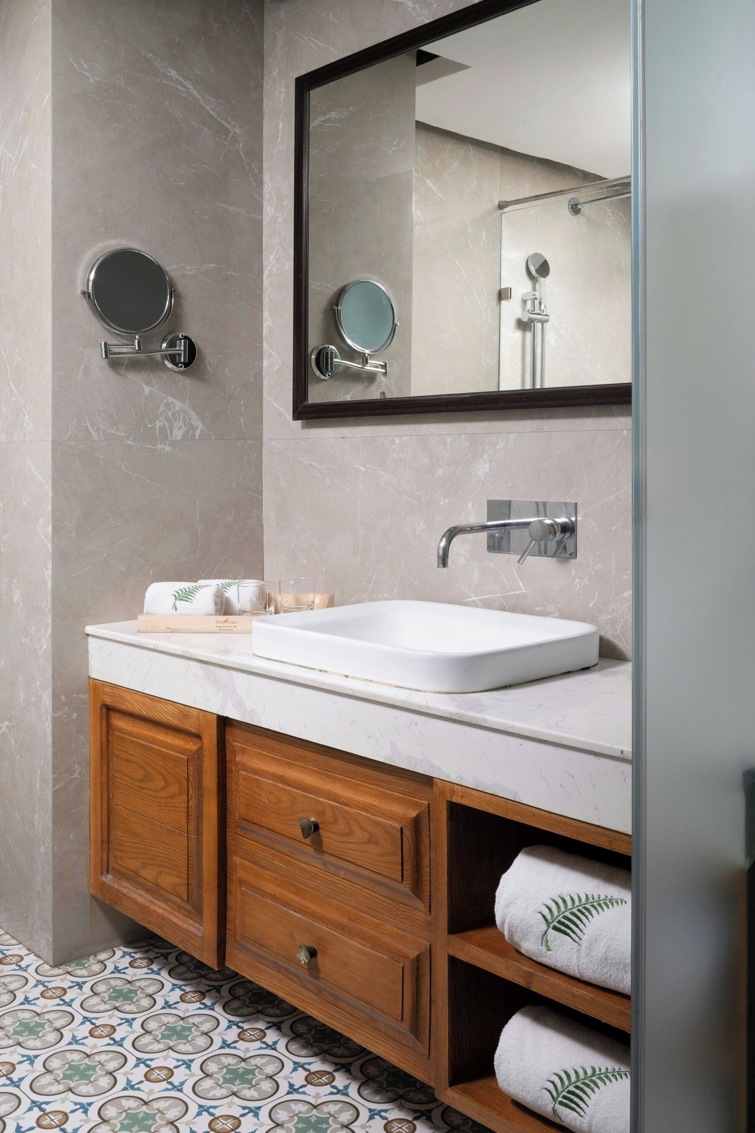 A bathroom with a marble wall, a white sink, wooden cabinets, and a mirror.