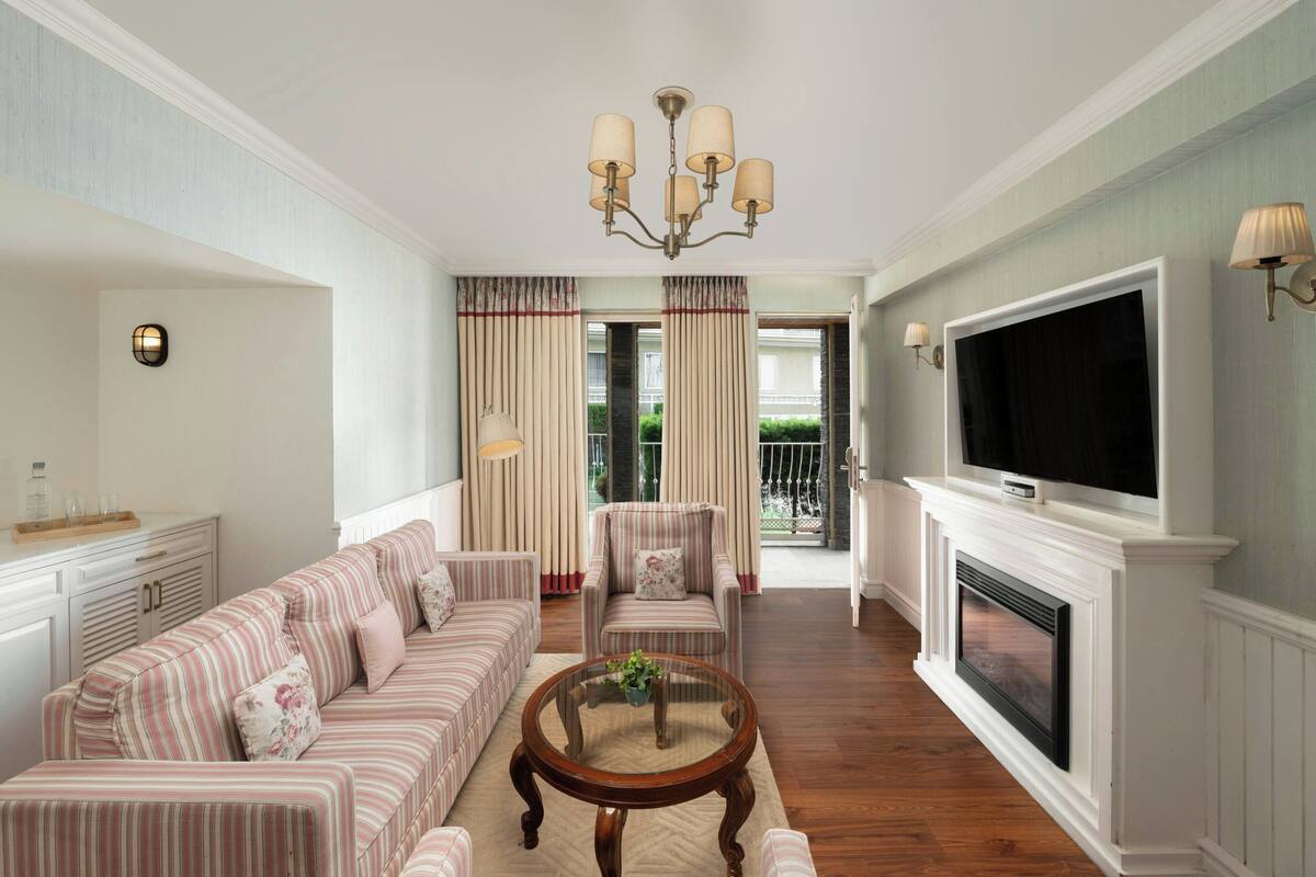 A living room with striped sofas, a glass coffee table, a fireplace, a television, and a chandelier.