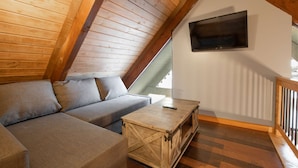 Ein Loft-Zimmer mit Holzbalkendecke, einer Couch, einem Couchtisch und einem an der Wand montierten Fernseher.
