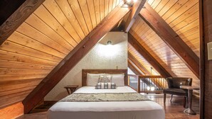 Ein gemütliches Schlafzimmer im Dachgeschoss mit geneigter Holzwanddecke, einem Bett mit weißer Bettwäsche und einem Sessel.
