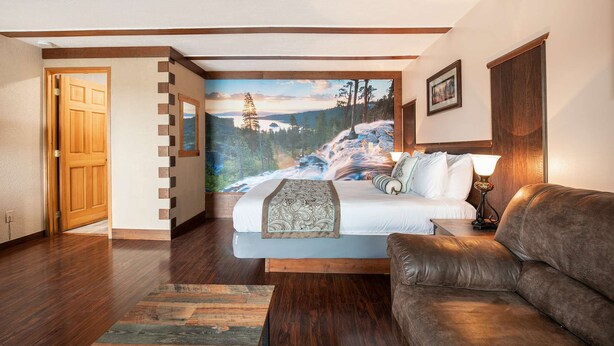 Ein Schlafzimmer mit einem großen Bett, einer Holztür, Blick auf einen Wald und einem braunen Ledersofa.
