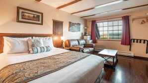 Ein Hotelzimmer mit einem großen Bett, einer Ledersofa, einem kleinen Tisch, einem Schreibtisch und einem Fenster mit Vorhängen.