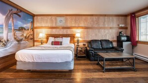 A hotel room with a bed, a desk, a chair, a TV, and a painting of a beach scene. - Salt Water Lagoon - Queen Studio Room at Wanderlust Inn, Pet Friendly (Ocean Shores)