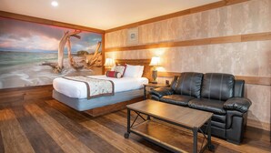 A hotel room with a bed, a leather sofa, a small table, and a mural of a beach scene. - Salt Water Lagoon - Queen Studio Room at Wanderlust Inn, Pet Friendly (Ocean Shores)