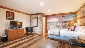 A hotel room with a bed, a TV, a wooden dresser, a chair, and a stone wall. - Salt Water Lagoon - Queen Studio Room at Wanderlust Inn, Pet Friendly (Ocean Shores)