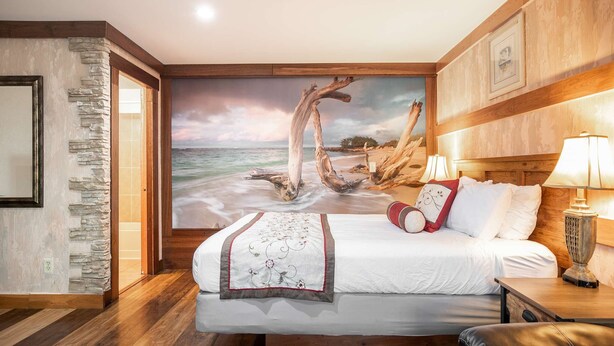A bedroom with a large beach mural, a wooden headboard, a bed with white linens, and a nightstand with a lamp. - Salt Water Lagoon - Queen Studio Room at Wanderlust Inn, Pet Friendly (Ocean Shores)