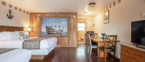 Habitación de hotel con dos camas, un escritorio de madera, un televisor y un cuadro grande de un barco.