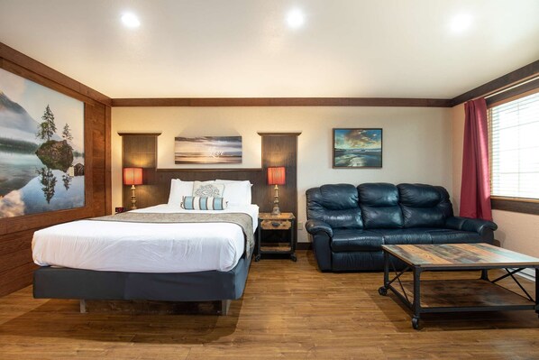 A hotel room with a bed, a leather sofa, a small table, and artwork on the walls. - Flip Flop - Queen Studio Room at Wanderlust Inn, Pet Friendly (Ocean Shores)