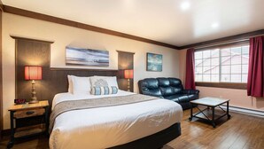 A hotel room with a large bed, a leather armchair, a small table, and artwork on the walls. - Flip Flop - Queen Studio Room at Wanderlust Inn, Pet Friendly (Ocean Shores)