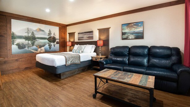 A hotel room with a bed, a black leather sofa, a wooden coffee table, and artwork on the walls. - Flip Flop - Queen Studio Room at Wanderlust Inn, Pet Friendly (Ocean Shores)