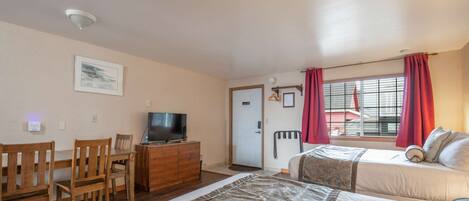 A room with a bed, a desk with a TV, a chair, and a window with curtains.