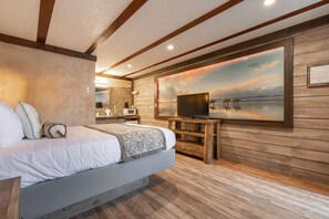 A bedroom with a bed, a TV, and a painting of a beach scene.