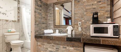 A bathroom with a stone wall, a sink, a mirror, a toilet, and a microwave.