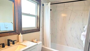 Een moderne badkamer met een marmeren douche, toilet en een wastafel met opbergmeubel.