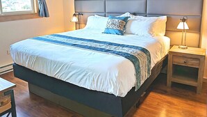 A modern bedroom with a large bed, wooden flooring, a grey padded headboard, and bedside lamps. - Sea Dreamer - 1 Bedroom Suite with 1 King and 1 Queen Bed at Wanderlust Inn, Pet Friendly (Ocean shores)