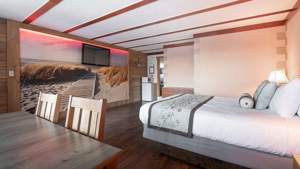 A bedroom with a bed, a TV mounted on the wall, a wooden dining table, and a breakfast bar. - Sea Dreamer - 1 Bedroom Suite with 1 King and 1 Queen Bed at Wanderlust Inn, Pet Friendly (Ocean shores)