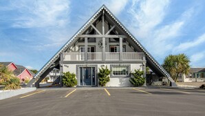 A modern two-story building with a triangular roof, a balcony, and a parking lot in front. - Ocean Song - Queen Studio Room at Wanderlust Inn, Pet Friendly (Ocean shores)