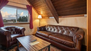 A cozy room with a leather sofa, two armchairs, a wooden coffee table, and a window with curtains. - Once Upon a Tide - Queen Studio Room at Wanderlust Inn, Pet Friendly (Ocean shores)