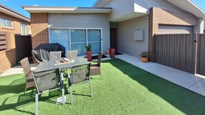 A backyard with a patio table and chairs, a barbecue grill, a potted plant, and a fenced area. - New Serene 4 bedroom home (Kambah)