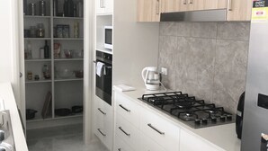 A modern kitchen with white cabinets, a gas stove, and a microwave. There is a coffee maker on the counter. - New Serene 4 bedroom home (Kambah)