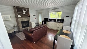 Un intérieur de chalet chaleureux avec une cheminée, un canapé en cuir, une table à manger et un coin cuisine.