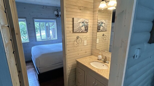 Une chambre avec un plafond en bois, un lit, une fenêtre et une salle de bain équipée d’un lavabo et d’un miroir.