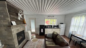 Un intérieur de chalet chaleureux avec une cheminée, un canapé en cuir, un coin repas et une cuisine.