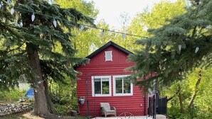 Une cabane rouge avec un porche, entourée d’une cour verdoyante et d’arbres.
