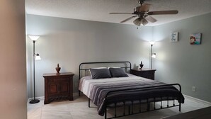 A bedroom with a bed, bedside tables, a ceiling fan, and wall-mounted lamps.