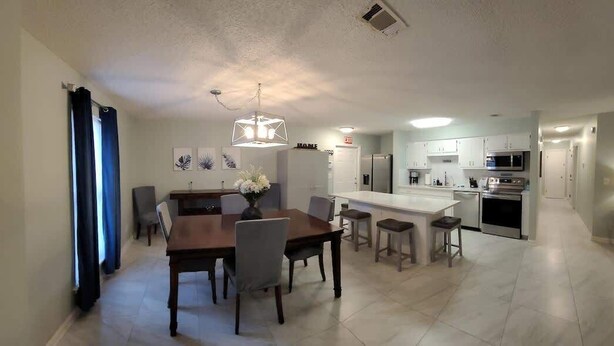 A modern kitchen with white cabinets, a central island, and a dining area with a wooden table and chairs.
