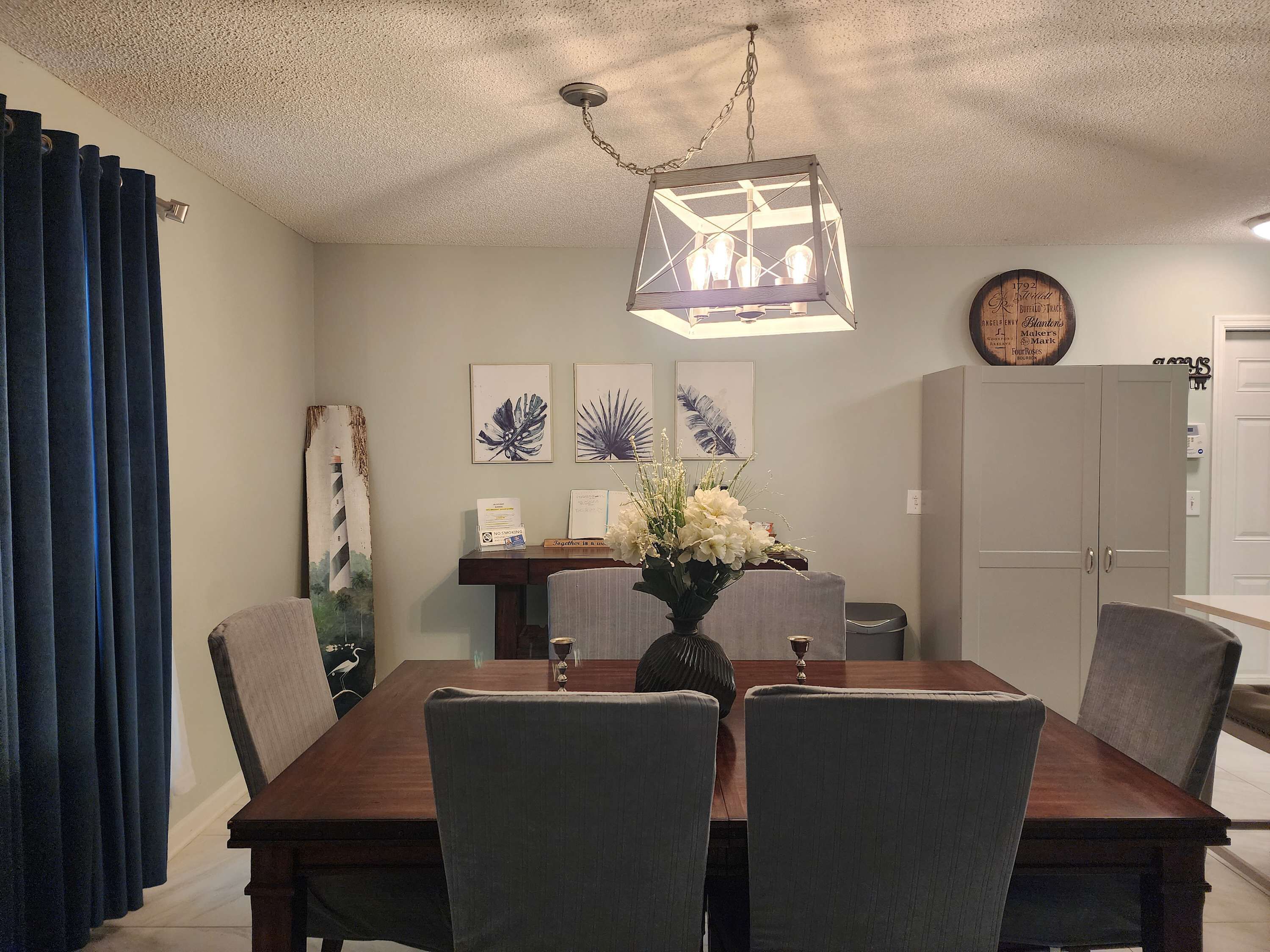 Een eetgedeelte met een houten tafel, grijs gestoffeerde stoelen, een decoratieve vaas met bloemen en een hanglamp.
