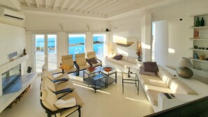 A modern living room with a sofa, armchairs, and a coffee table. There are large windows with a view of the sea. - La Vue-Boule (Paros)