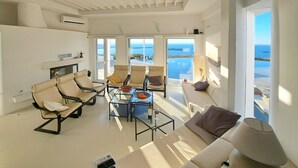 A spacious living area with a sofa, chairs, a coffee table, and a TV. Large windows offer a view of the sea. - La Vue-Boule (Paros)
