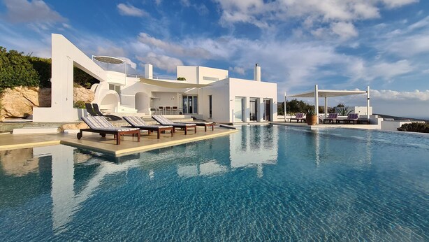 A modern pool area with lounge chairs, a clear blue pool, and a white building with large windows and a covered seating area. - La Vue-Boule (Paros)