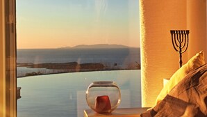 A fishbowl with a single fish on a windowsill, a menorah on a wall, and a view of a body of water and distant land. - La Vue-Boule (Paros)