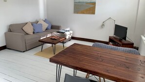 Una sala de estar con una mesa de comedor de madera, un sofá, una mesa de centro, un televisor y un cuadro en la pared.