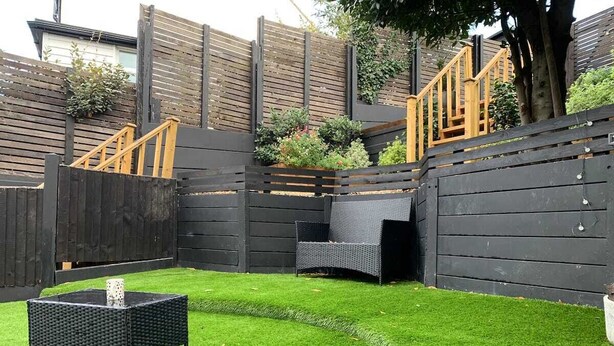 Un patio con césped artificial, una mesa de mimbre y una silla de mimbre.