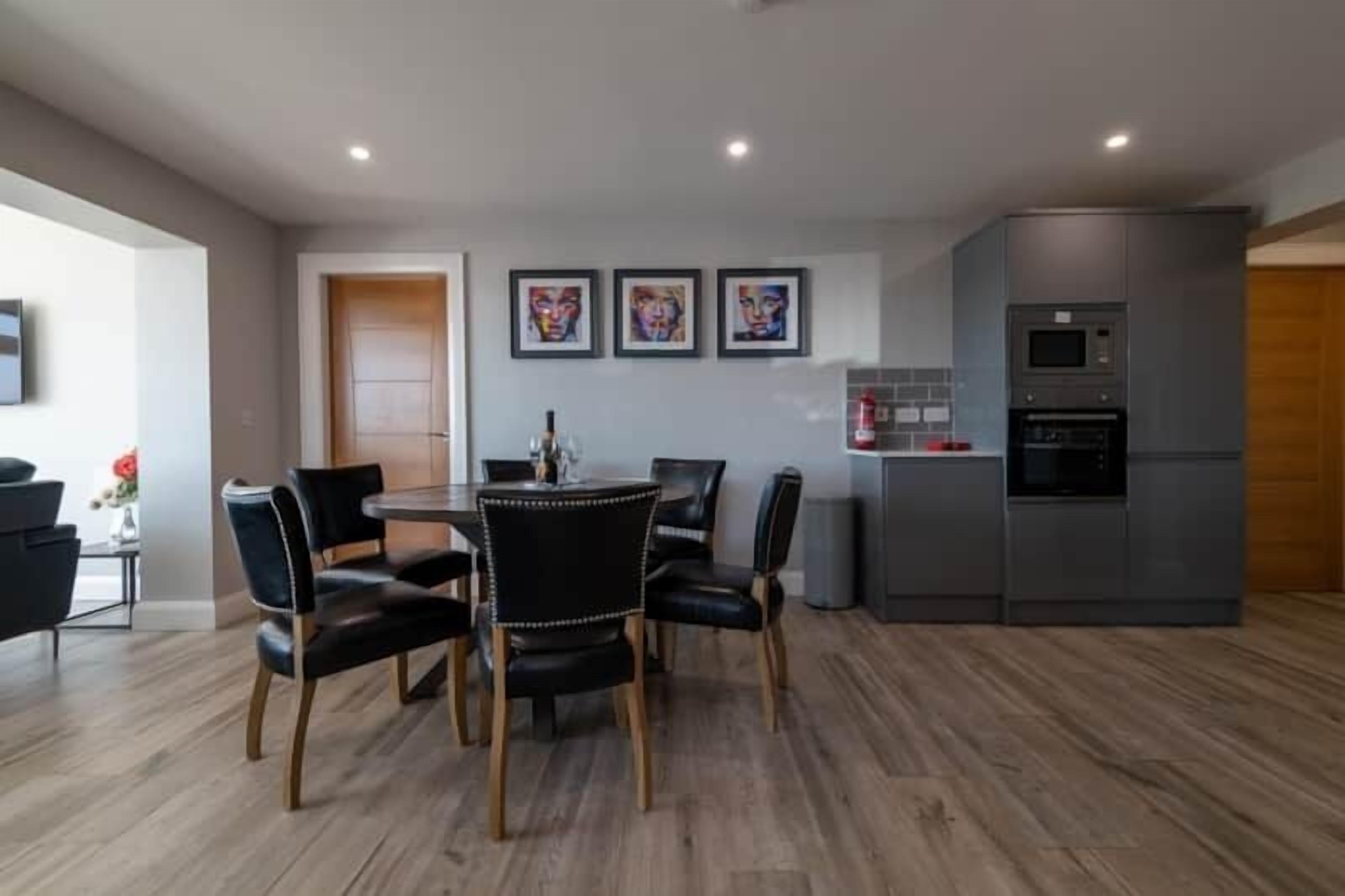 A modern kitchen with a built-in oven and microwave, a dining area with a round table and chairs, and three framed artworks on the wall.