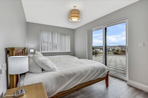 Un dormitorio moderno con una cama grande, una mesita de noche con lámpara, una ventana con persianas y vistas al exterior.