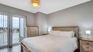 Ein Schlafzimmer mit einem großen Bett, einem Nachttisch, einer Kommode und Blick durch eine Glastür.