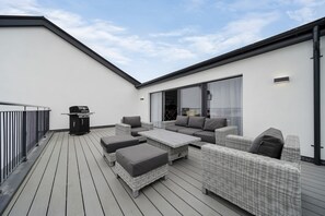 A rooftop patio with wicker furniture, a barbecue grill, and a sliding glass door leading to an indoor area. - Bayview Downings- Luxury 3 Bedroom First Floor Apt (Downings)