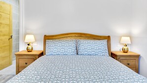 Une chambre à coucher avec une tête de lit en bois, deux tables de chevet avec des lampes, une couvre-lit à motifs et une porte en bois.