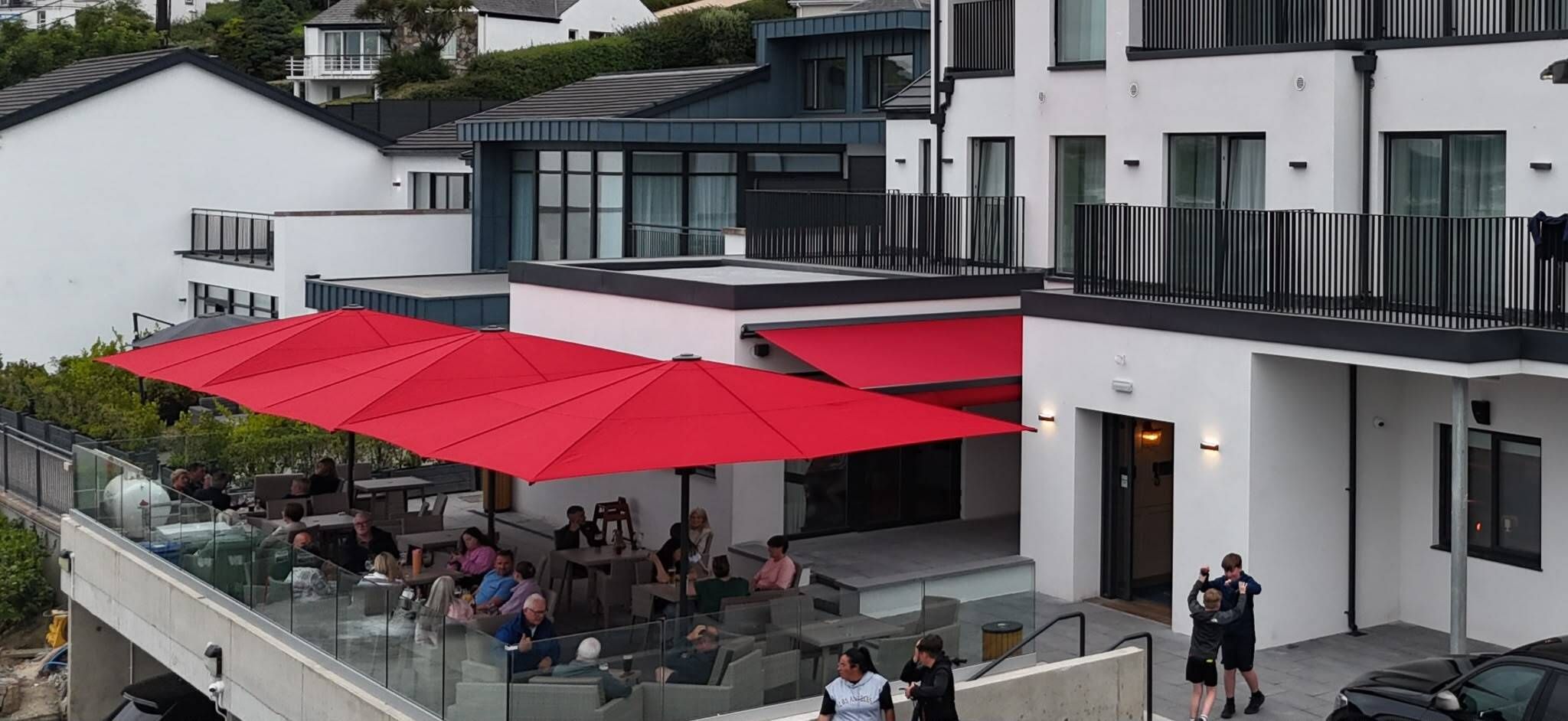 An outdoor seating area with red umbrellas, glass railings, and people dining.