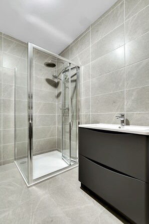 Un baño moderno con cabina de ducha de vidrio, tocador oscuro y paredes con azulejos.
