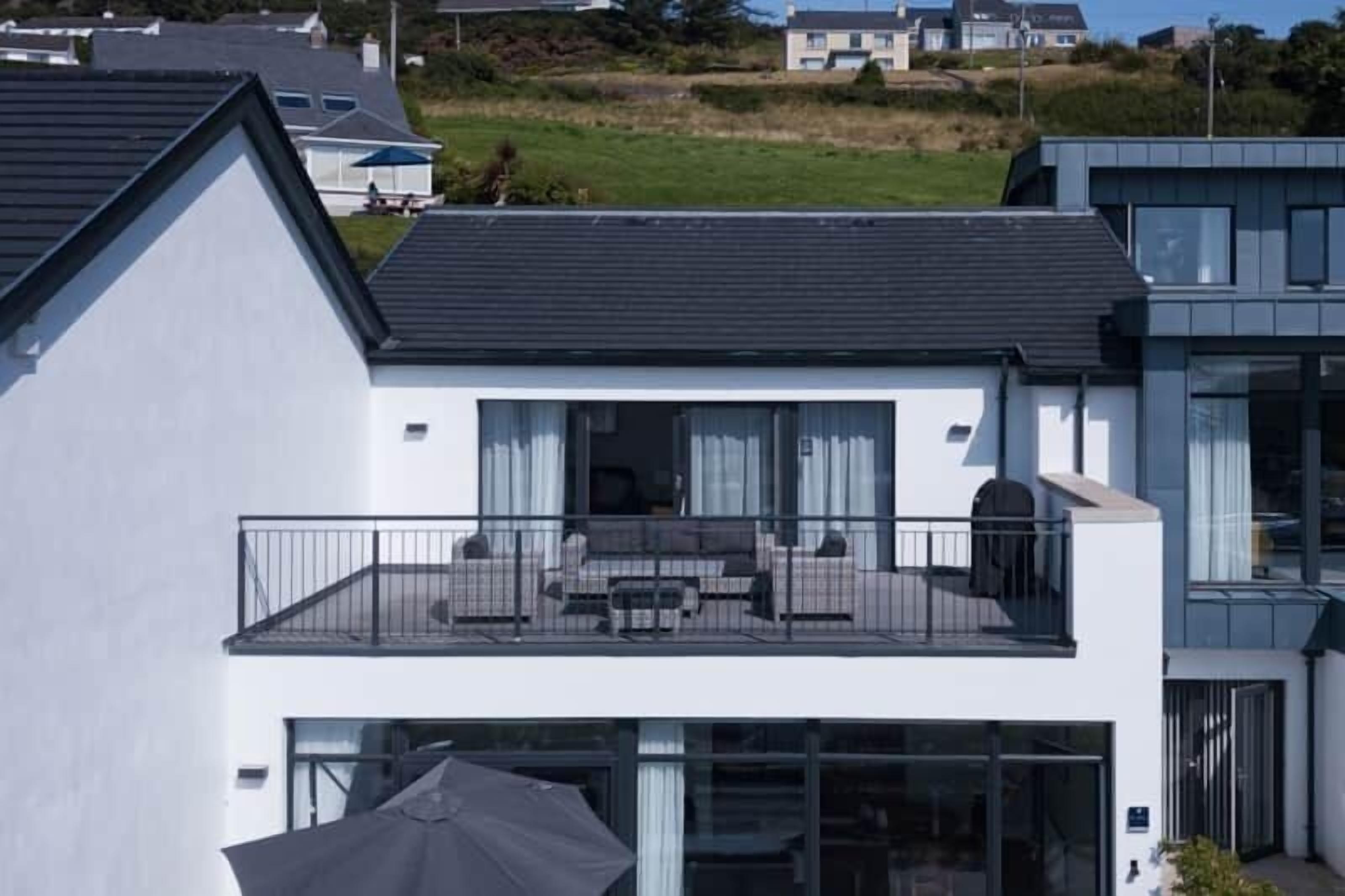 A modern two-story house with a balcony, large windows, and a flat roof.
