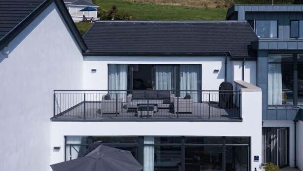 Une maison moderne à deux étages, dotée d’un balcon, de grandes fenêtres et d’un toit plat.